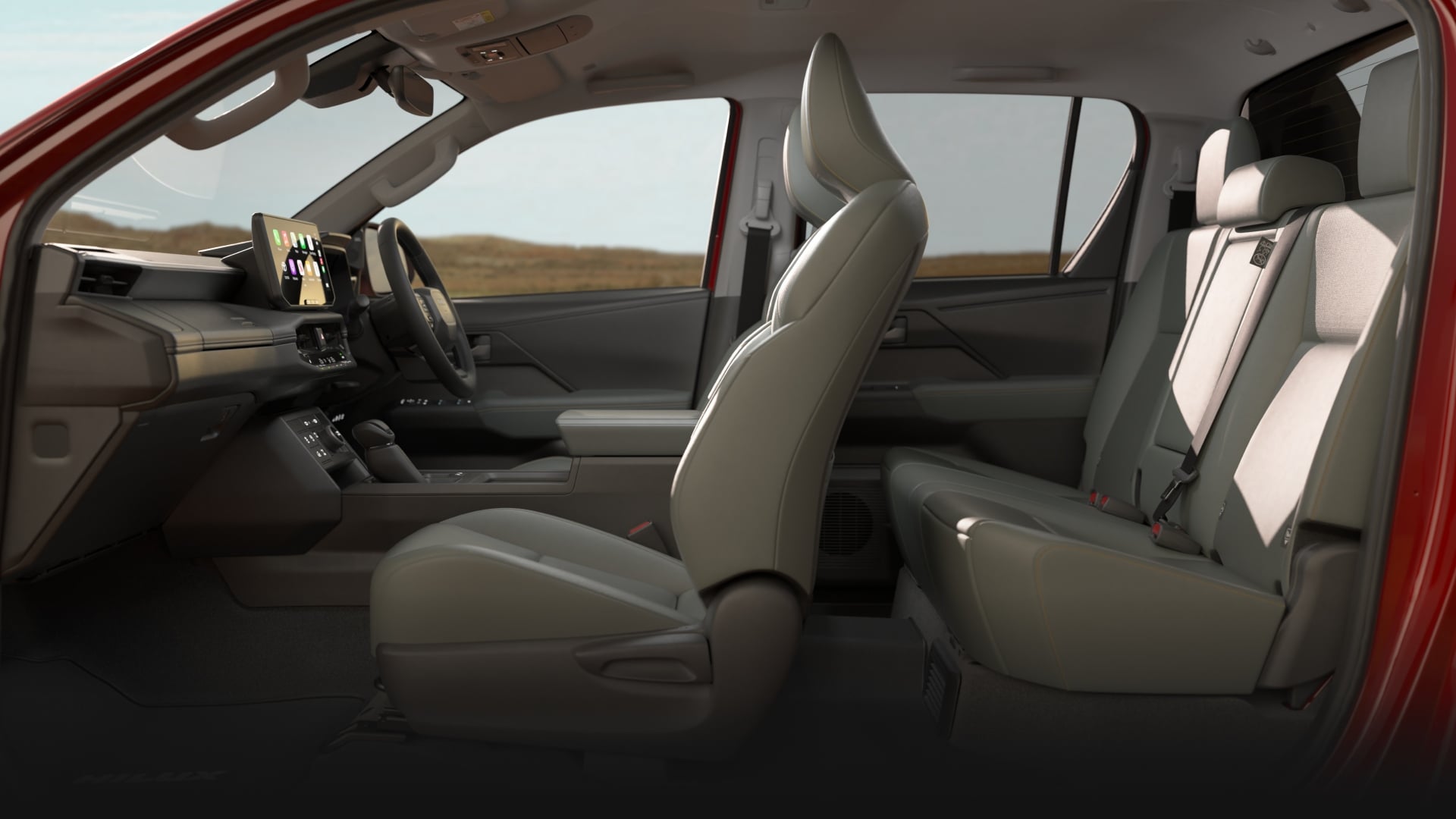 The interior of a Feverish Red HiLux Rogue with mineral-coloured leather-accented seats. Late afternoon sun filters through the windows, and the double-cab configuration with front and back seats is clearly visible.