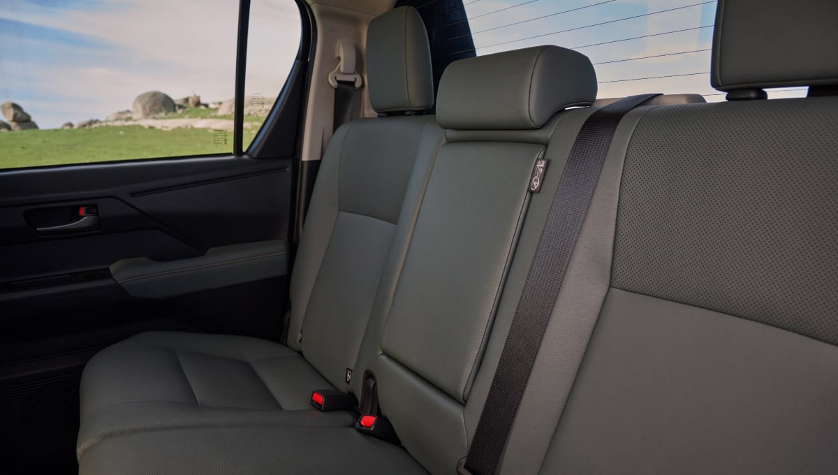 The interior back seats of a HiLux double-cab ute, trimmed with dark fabric. Green grass and a cloudy blue sky are visible out the windows.