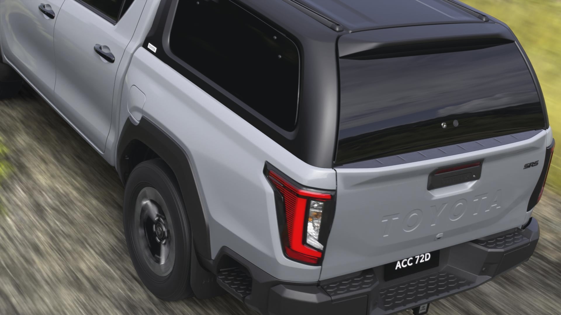 A rear view of a Stunning Silver HiLux double-cab ute, a canopy with lift-up windows fitted to it. On the road below, a slight motion blur conveys speed.