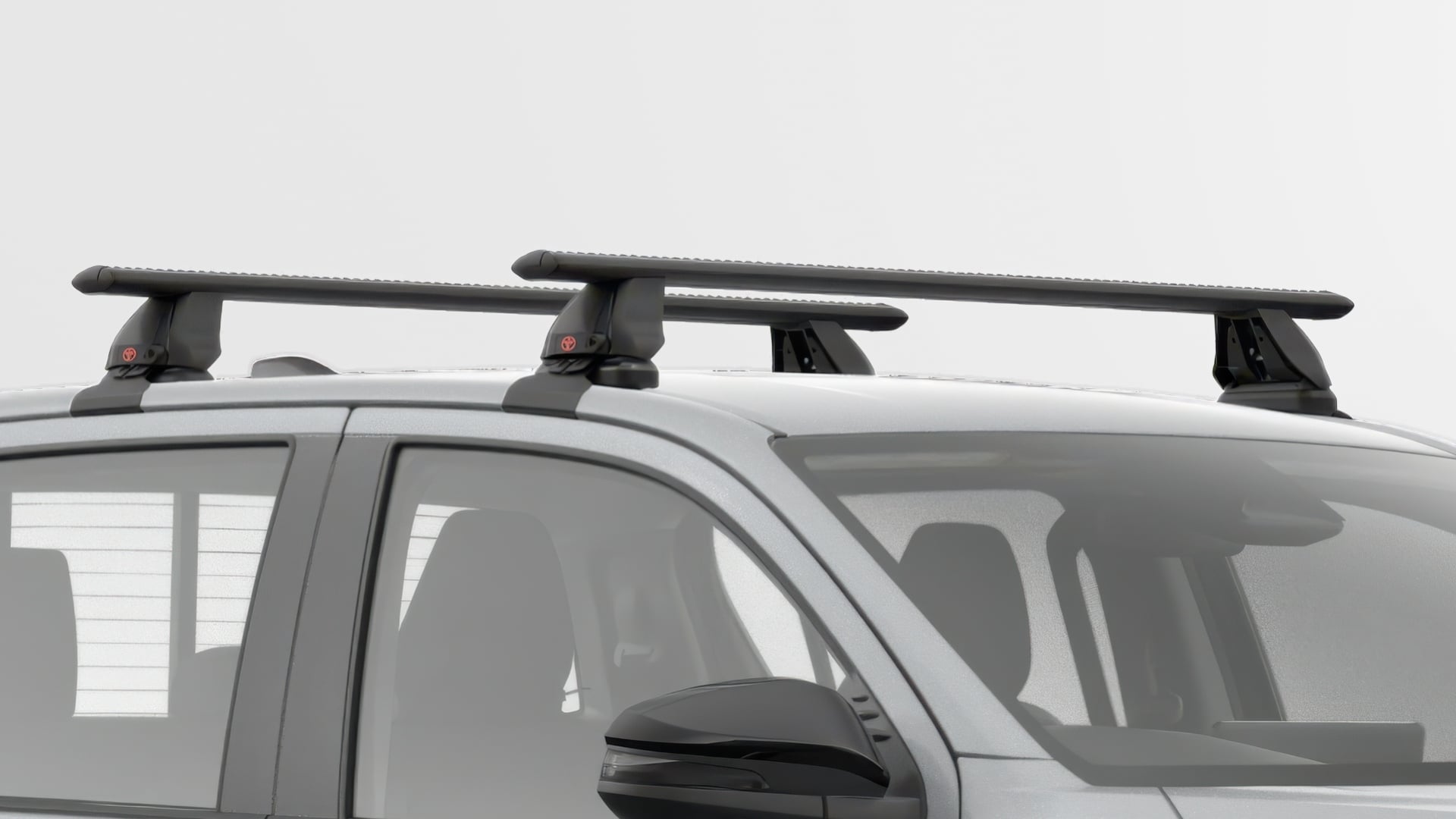 A Stunning Silver Toyota HiLux SR5 double-cab ute is shown in a studio setting. It is fitted with a set of two black Aero Roof Racks mounted on the roof. The background is plain white.