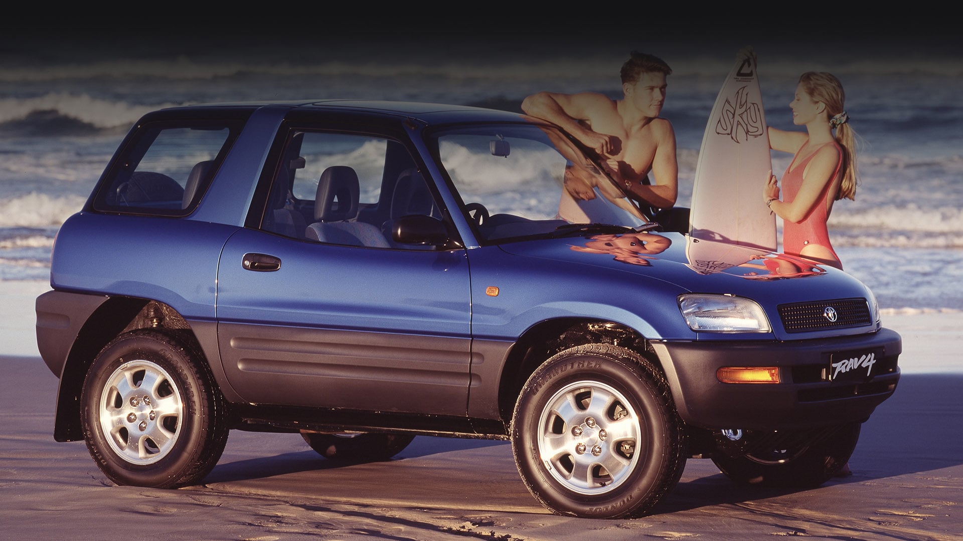 A retro advertising image of a blue, 1994 Toyota RAV4 parked on the sand beside the ocean. Two surfers stand beside it chatting, the man leans up against the vehicle and the woman holds a white surfboard.