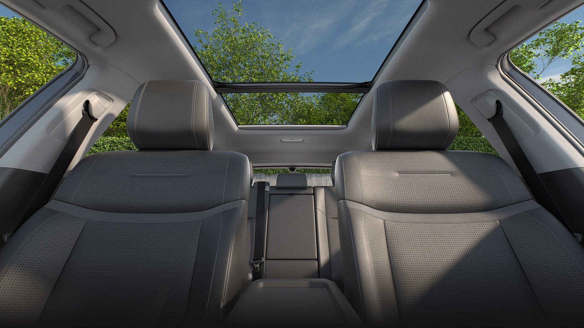 A low angled view of the RAV4’s fabric-trimmed  front passenger seats. Leafy green trees and blue skies are visible through the panoramic roof.